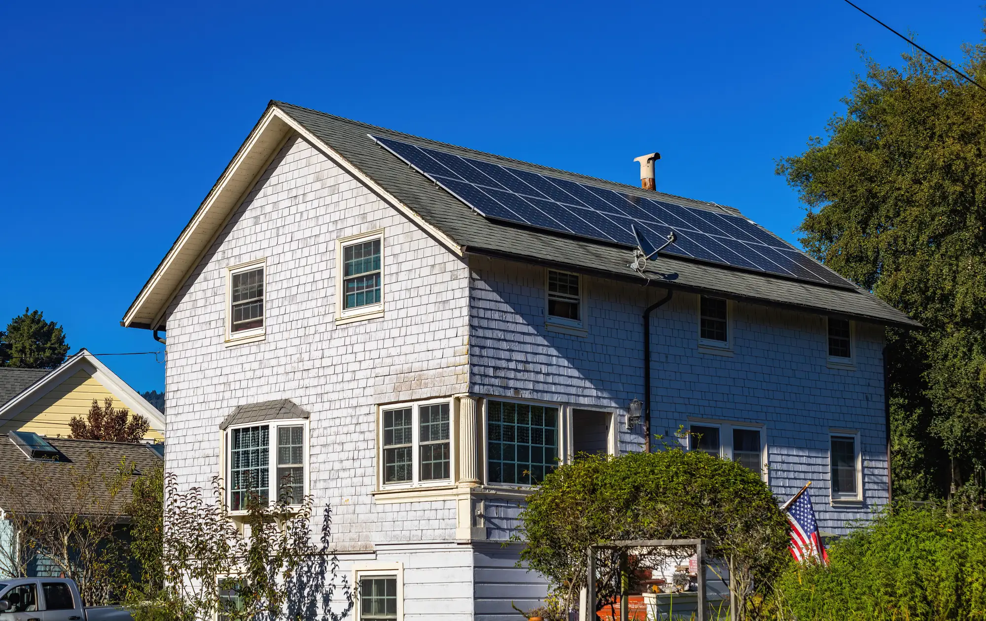 A shingled two-story house seen from the street, a solar array across the slope of its roof